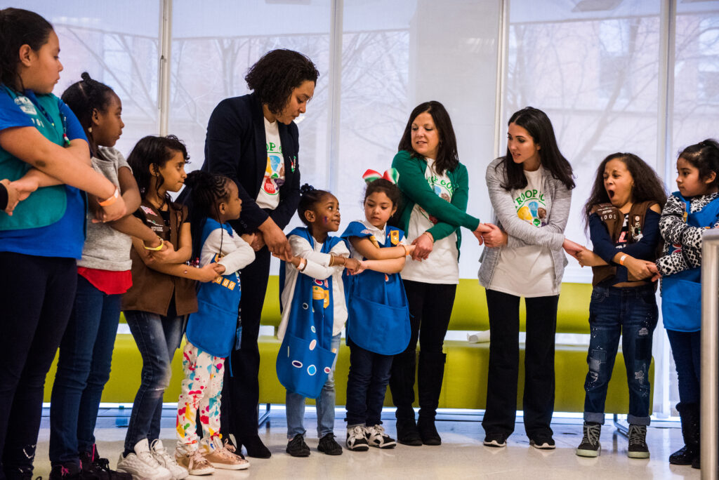 A group of Girl Scouts stand in a circle holding hands.